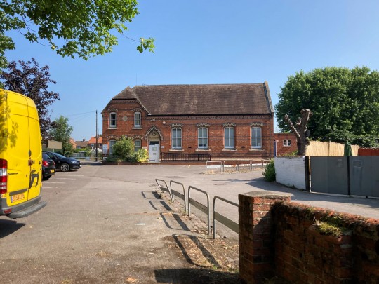 View from the right of the site entrance - Frontage of existing building set back, car parking spaces are situated to the left and site entrance situated to the right.